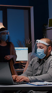 在公司办公室工作的工作狂商人，戴着面罩和面罩，抵御 covid19