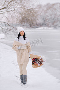 一个穿着米色开衫和冬花的女孩在下雪的季节在大自然中漫步。