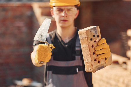 建筑工人穿着制服和安全设备站在建筑物上拿着砖块和工具的画像