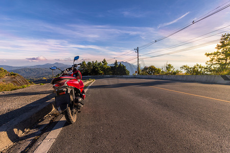 摩托车、蜿蜒的道路、背景上的山脉和日落时的蓝天。