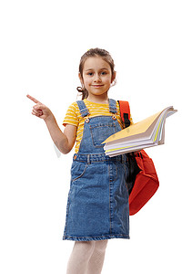女学生，一年级学生拿着书，用手指指着白色背景上的复印空间，微笑着，看着相机