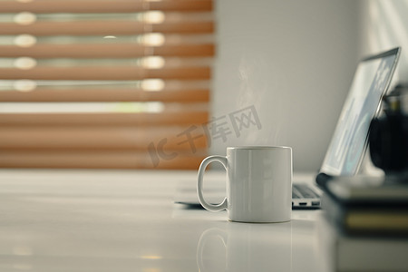 清晨的阳光下，白色办公桌上放着一杯热咖啡。