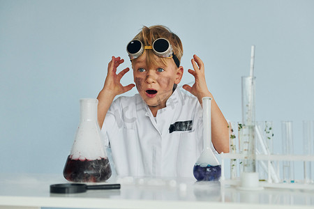 穿着外套的害怕的小男孩用设备在实验室里扮演科学家