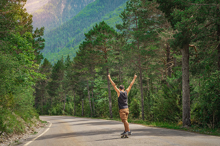 时髦的家伙与长板张开双臂享受生活在山路和美丽的风景。