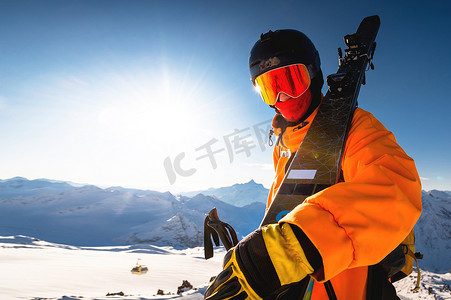 一名运动员戴着头盔和面罩，肩上扛着滑雪板的照片。