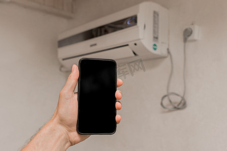 一个人的手拿着一部手机或智能手机，上面有黑色的文字和设计屏幕，背景是房子房间墙上的空调