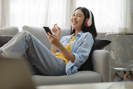 年轻女子在家里使用智能手机听音乐。