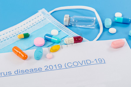 新型冠状病毒感染预防要点摄影照片_蓝色背景上带有疫苗和药丸的 2019 年冠状病毒病