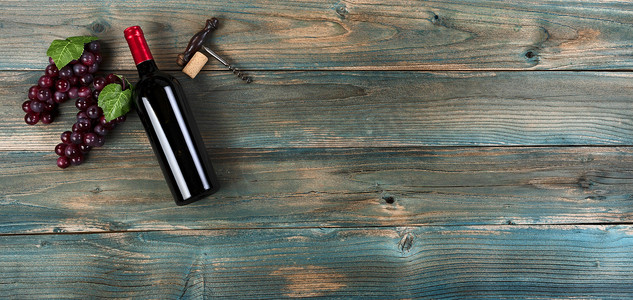 红酒背景，瓶、葡萄和开瓶器在褪色的蓝色木头上