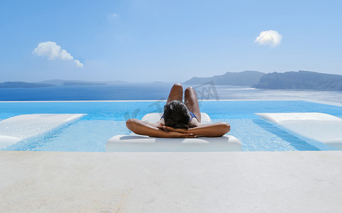 在圣托里尼度假的年轻亚洲女性在游泳池放松，俯瞰火山口海洋