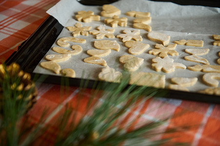 气氛金色摄影照片_透过模糊的冷杉针叶和金色松果，可以看到带有姜饼面团雕刻模具的烤盘