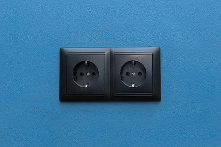 蓝墙背景上的双黑插座供电家庭能源供应电力，特写