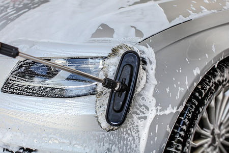 新店开业洗车摄影照片_在自助洗车中用刷子清洗的银色汽车前灯。