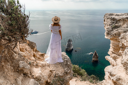 一位头发松散、身穿白色长裙的女孩从黄色岩石间的楼梯上走下来，俯瞰着大海。