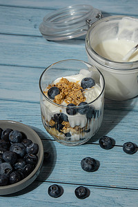 增强免疫力摄影照片_早上格兰诺拉麦片早餐配自制希腊酸奶，蓝色木制背景眼镜中的蓝莓。