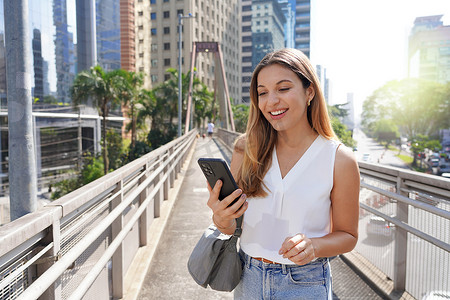 巴西圣保罗现代可持续发展大都市人行天桥上微笑的女孩看着她的智能手机的肖像