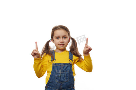 穿着黄色毛衣和蓝色牛仔服的可爱小女孩，用手指指着白色背景中的复制空间