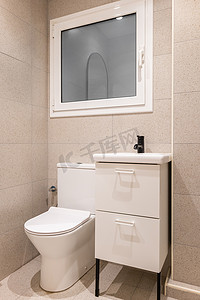 家居洗手间摄影照片_部分浴室配有马桶、木制家具上的洗脸盆和米色瓷砖墙壁