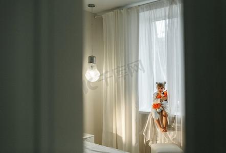 一个穿着浴袍的女孩在窗台上玩着一只针织狮子