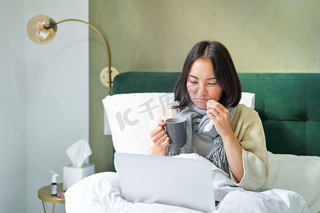 勤劳的亚洲女孩因感冒躺在床上，感染流感，但在家用笔记本电脑工作，一边生病一边学习