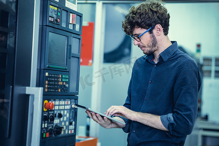 年轻工程师美国专业工作人员使用平板电脑操作先进机器。