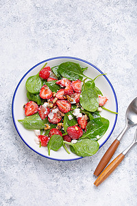 清淡健康的夏季沙拉，配以新鲜草莓、菠菜、奶油奶酪和核桃，放在白色陶瓷盘子上，上面是白色质朴的石头背景。
