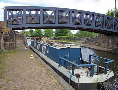 一座蓝色的人行桥穿过西约克郡布里格豪斯的考尔德和赫布尔运河，下面停泊着旧的窄船