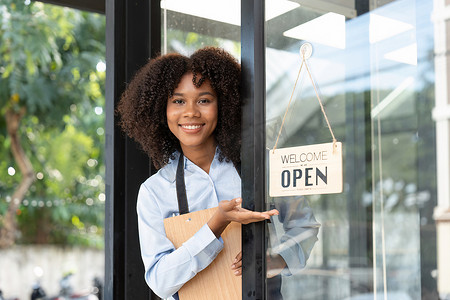 新店开业限时特惠摄影照片_小企业非洲女老板面带微笑，同时转向咖啡馆开业的标志。