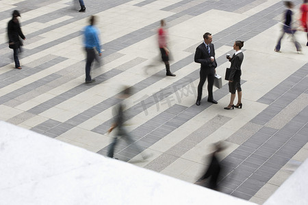 站在高处的男人摄影照片_商人和女商人站在户外广场交谈，人们经过高处的视野