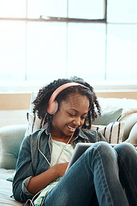 数字平板电脑、沙发和戴着耳机的女孩一边听音乐、收音机或播客一边放松。