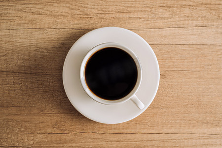 碟子俯视图摄影照片_平躺的黑咖啡放在一个白色的杯子里，木桌上放着一个碟子