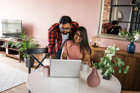 技术远程工作和生活方式概念 — 戴眼镜、带笔记本电脑在家办公室工作的快乐印度男女