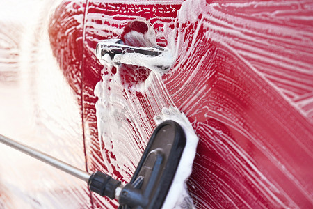 在自助洗车中洗过的红色汽车，刷子上的细节在侧门上留下笔触，宽横幅，文本左侧有空白空间