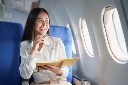 亚洲商务女性乘客坐在商务舱豪华飞机上，同时使用笔记本书工作，同时旅行概念