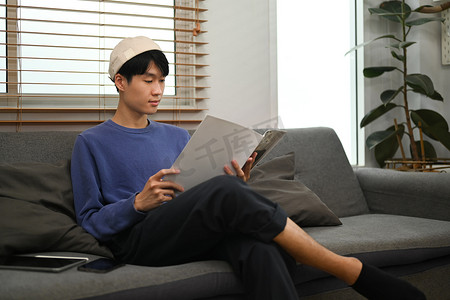 安静的亚洲年轻人在沙发上放松，看书，在家度过闲暇时光
