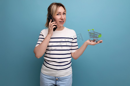 横幅女购物者在蓝色背景上拿着带复印空间的购物手推车通过电话下单的照片