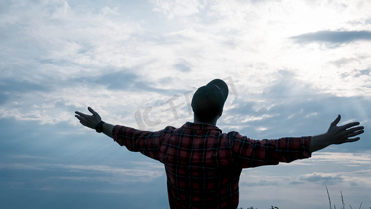 一个年轻人仰望天空，双手放在一边，那个人假装是一架飞机，一道美丽的风景和一个人的轮廓，特写。