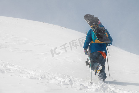 滑雪设备和滑雪板的人爬上一座雪山。