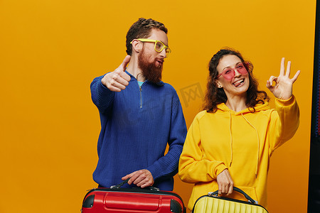 广告黄色摄影照片_女人和男人微笑着，手里拿着手提箱，黄色和红色的手提箱愉快地微笑着，弯曲着，黄色背景，去旅行，家庭度假旅行，新婚夫妇。