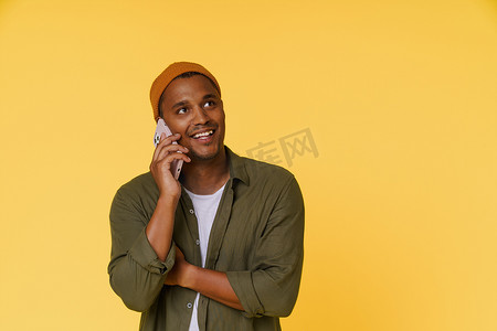戴着橙色帽子的微笑非洲男子正在打电话，黄色背景上有复印空间。