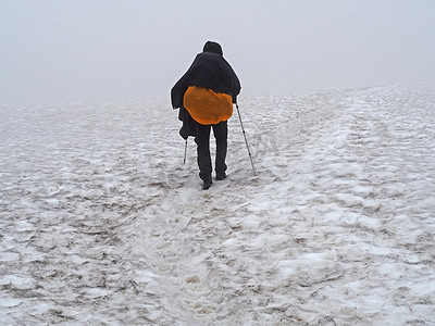 男子徒步旅行者背着沉重的背包和追踪杆在雪地上的乳白色薄雾中行走在夏季的冰岛跋涉中