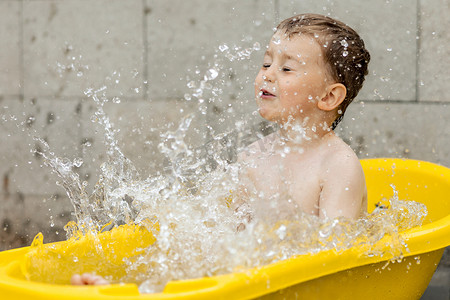 小男孩在洗澡摄影照片_可爱的小男孩在户外的黄色浴缸里洗澡。