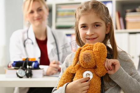 倾听和学习摄影照片_诊所里有玩具和听诊器的医生和孩子