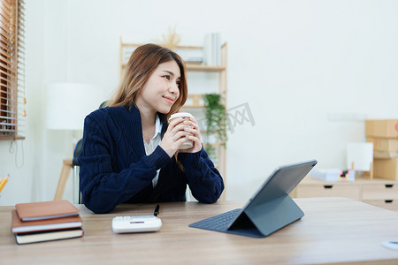 一位亚洲女商人一边喝咖啡一边使用电脑和办公桌上的财务报表文件的肖像