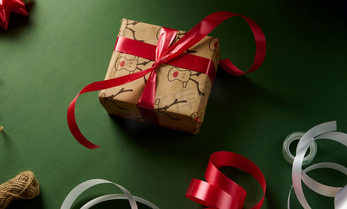 端午节礼摄影照片_顶视图圣诞礼品盒，包裹在装饰性包装纸中，在绿色背景上用一条红色闪亮的丝带绑起来。