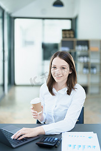 一张亚洲女商人的画像，在休息时，脸上挂着快乐的笑脸，手里拿着一杯咖啡