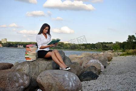 拿着书的女孩坐在海边的岩石上