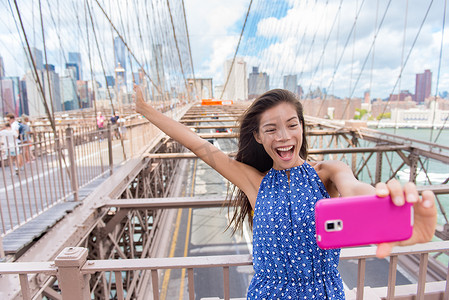 快乐的自拍女游客在纽约布鲁克林布里奇用手机拍有趣的照片