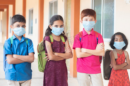 戴着医用面具、背着书包的孩子们双臂交叉地站着，看着镜头 — 返校和重新开学的概念。
