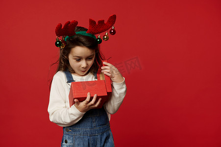 惊讶的白人女婴戴着鹿角环，在打开装有圣诞礼物的礼盒时表达幸福